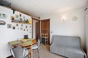 A dining area with a wooden table, chairs, and a sofa. There are wall-mounted shelves with decorative items and a door leading to another room. - Casa Pepe Apartment with Sea View, Garden, and Wi-Fi (Imperia)