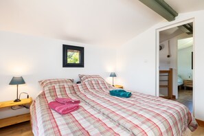 A bedroom with a bed, two bedside lamps, a framed picture on the wall, and a wooden bench.