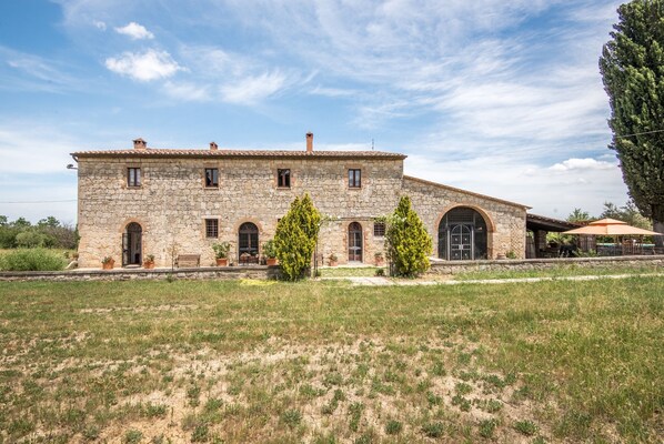 A stone building with arched windows and a sloped roof, surrounded by grass and trees.