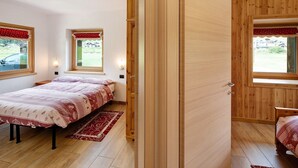 A bedroom with a bed, a wooden wardrobe, a window with a view, and a door.