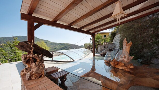 A covered outdoor seating area with a glass table, wooden bench, and a view of a mountain landscape. - Holiday Apartment "Villa Lice - Coronata" with Mountain View, Shared Pool & Wi-Fi (casarza ligure)