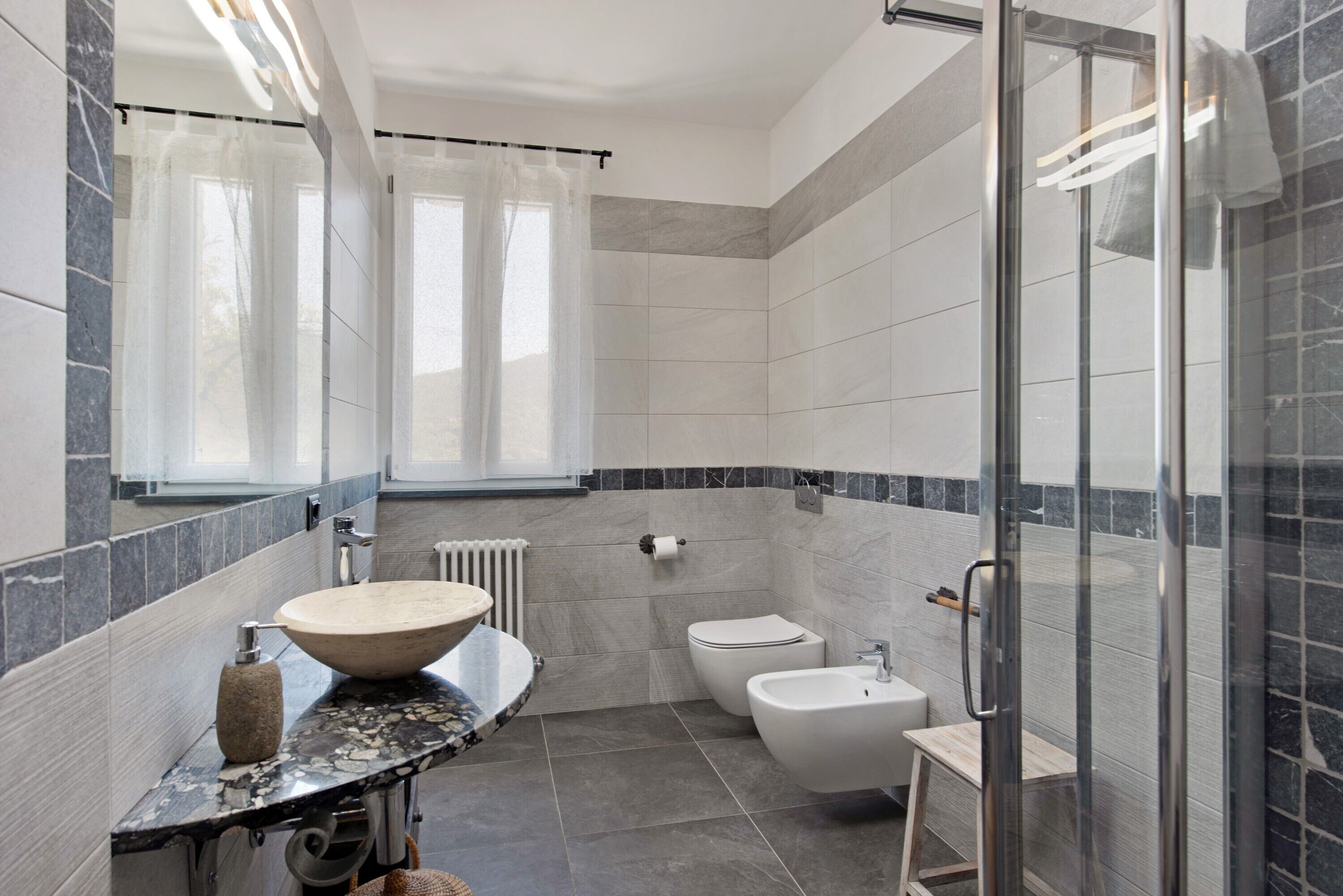 Een moderne badkamer met een marmeren wastafel, toilet, bidet en een douche met glazen wanden.