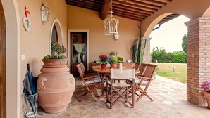 An outdoor patio with a wooden table, chairs, terracotta pots with flowers, and a pergola with hanging lights. - Incredible Villa in the Heart of Tuscany (Cecina)