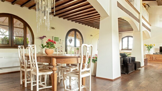 A spacious dining area with a wooden table and chairs, a chandelier, and a view of the outdoors through large windows. - Incredible Villa in the Heart of Tuscany (Cecina)