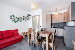 A modern kitchen with wooden cabinets, a dining table with chairs, a red sofa, and decorative wall art.
