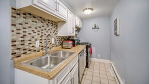 Una cocina con armarios blancos, salpicadero de azulejos, pileta de acero inoxidable, un tostador y una estufa.