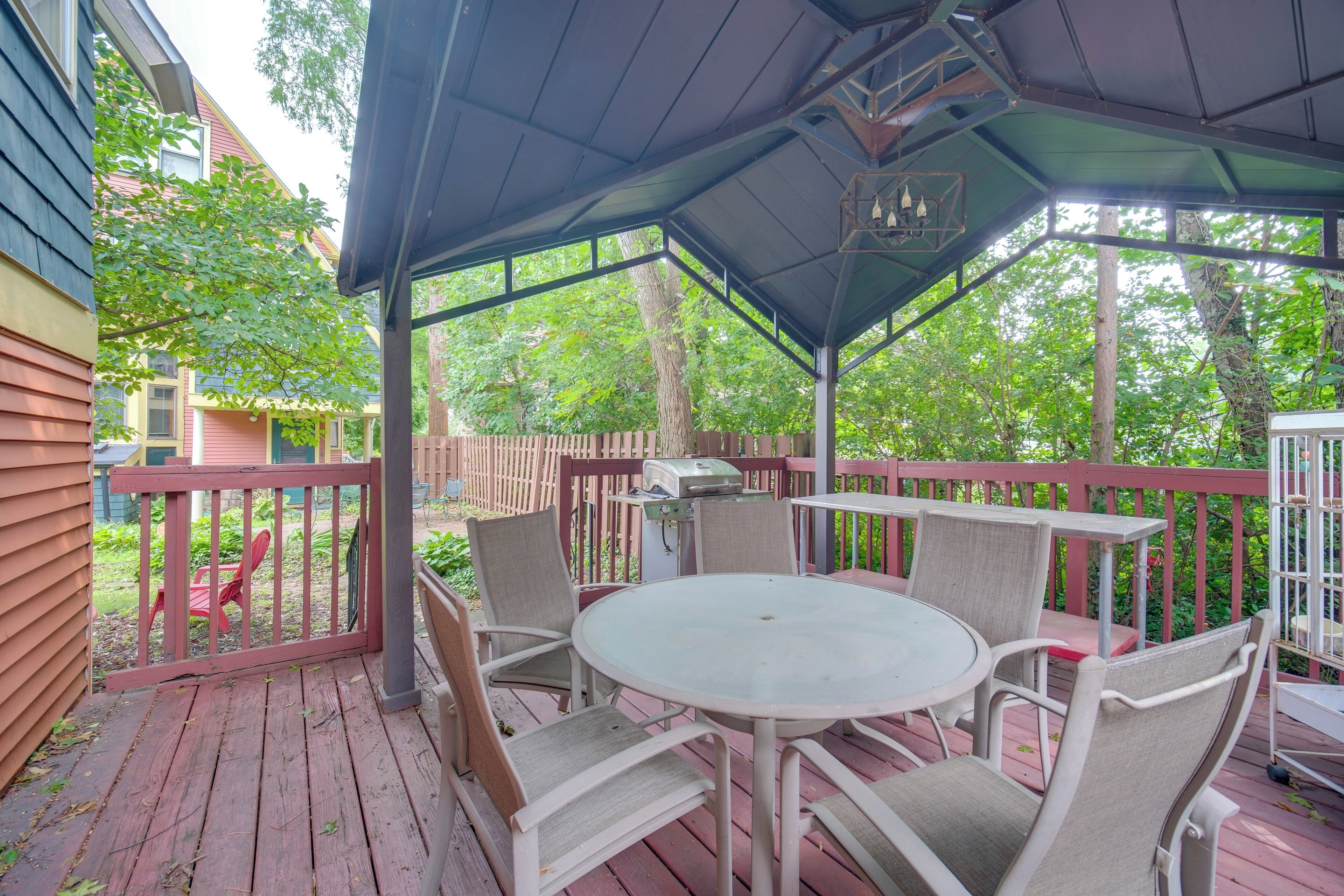 A covered outdoor patio with a round table and chairs, surrounded by a wooden deck and a metal railing.