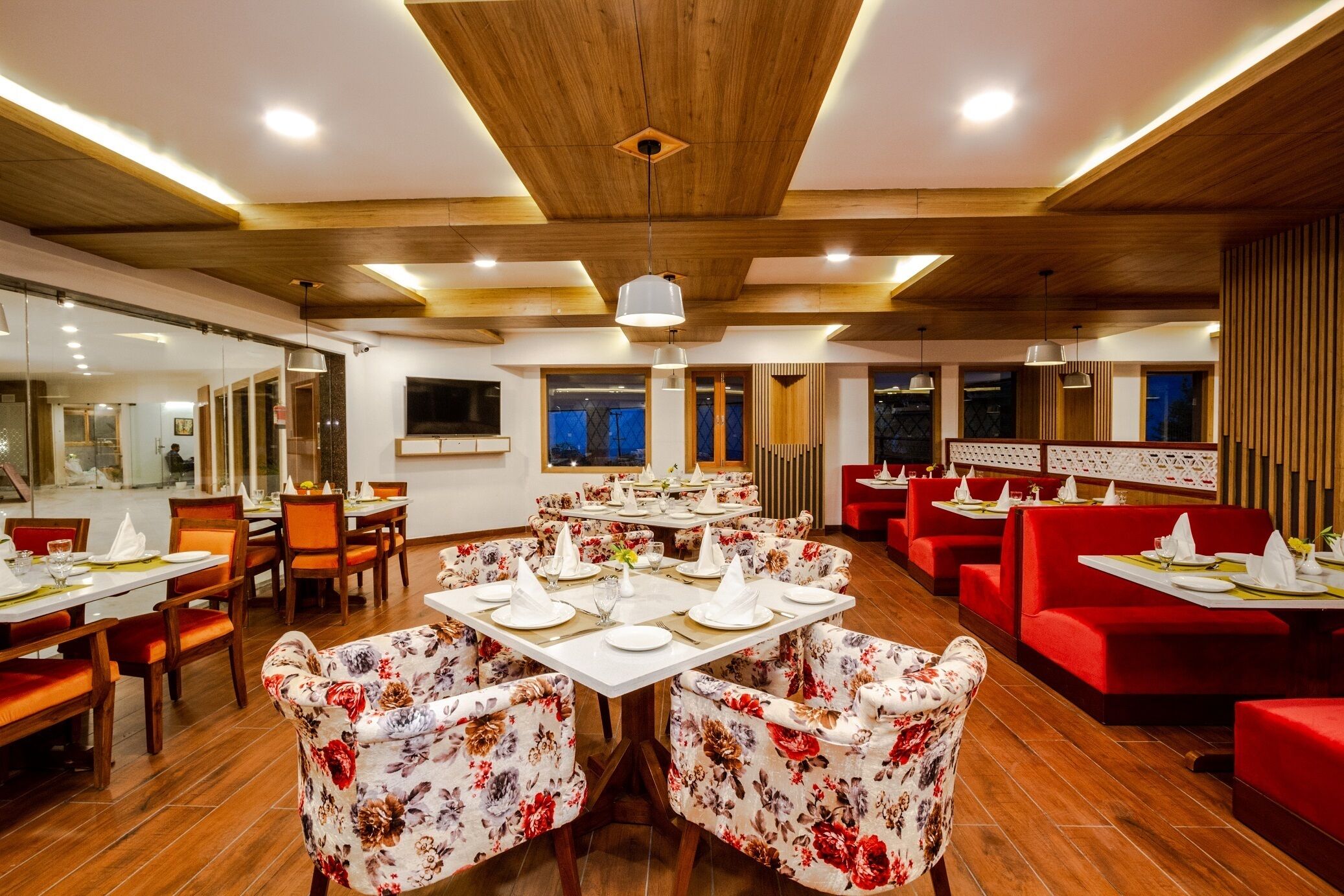 A restaurant with wooden ceiling beams, red upholstered booths, and floral-patterned chairs. Tables are set with white tablecloths and napkins.
