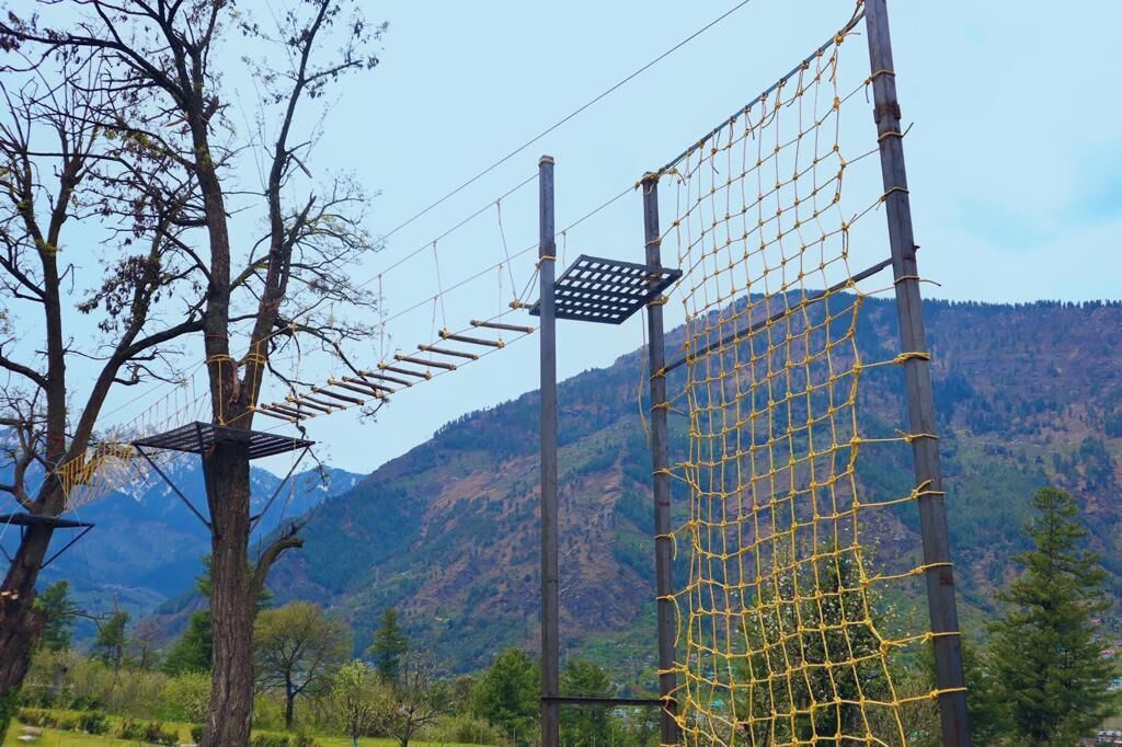 Un parcours d’obstacles en plein air, composé de structures en filet et de plateformes en bois, le tout situé dans un cadre montagneux.