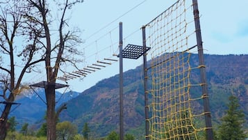 Un parcours d’obstacles en plein air, composé de structures en filet et de plateformes en bois, le tout situé dans un cadre montagneux.