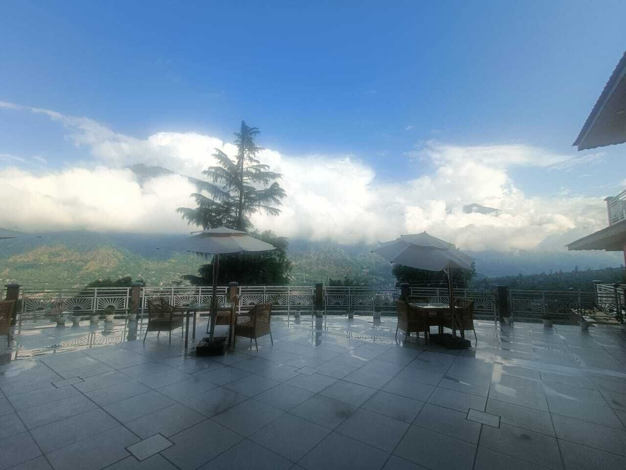 An outdoor terrace with tables and chairs, a railing, and a view of a mountain range.