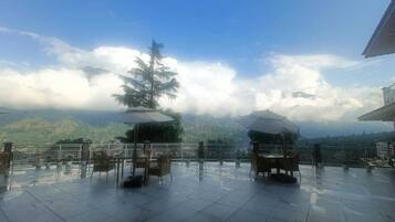 An outdoor terrace with tables and chairs, a railing, and a view of a mountain range.