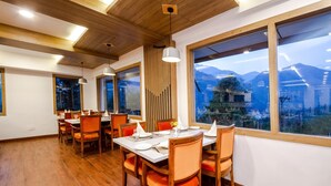 A dining area with wooden tables and chairs, large windows with a mountain view, and a wooden ceiling. - Anand Vardhan Resorts (Kullu)