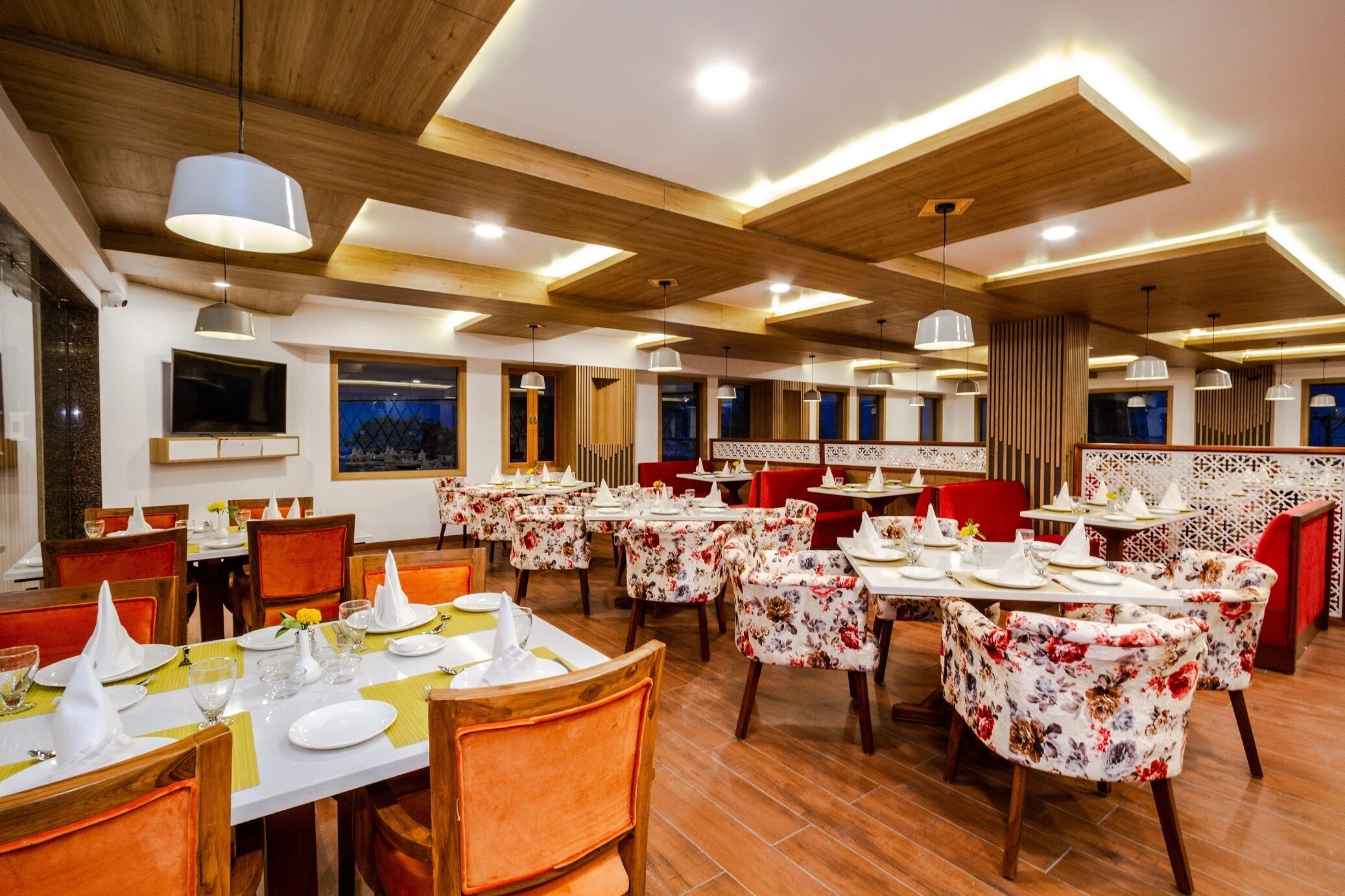 A restaurant with multiple dining tables, wooden ceiling beams, and red chairs.