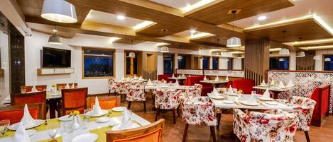 A restaurant with multiple dining tables, wooden ceiling beams, and red chairs.