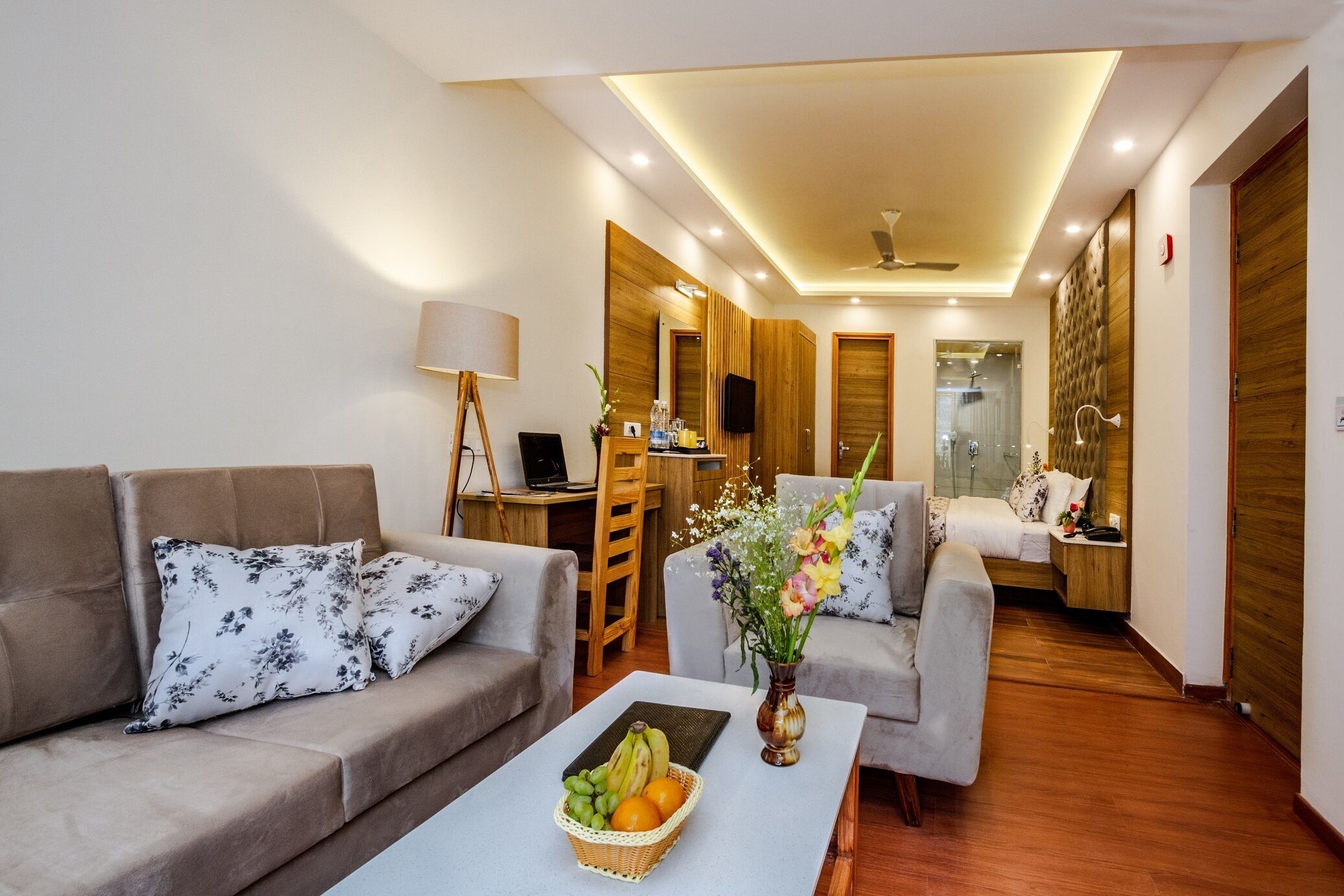A modern living room with a sofa, a coffee table with fruit and flowers, a desk with a computer, and a TV.