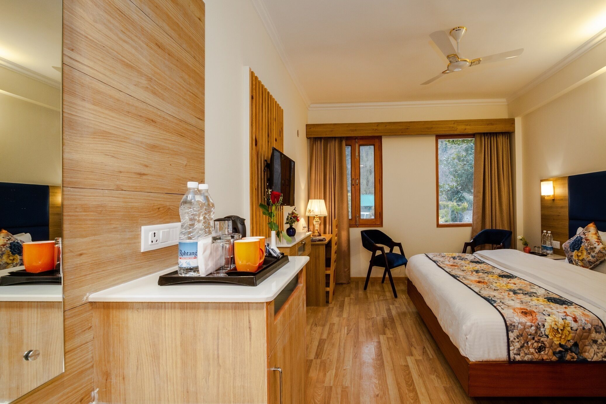 Une chambre d’hôtel avec un meuble en bois, un lit recouvert d’une courtepointe à motifs floraux, un bureau avec une lampe et une fenêtre avec des rideaux.