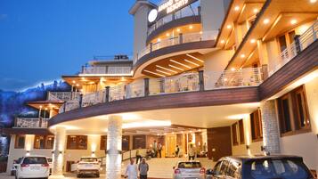 Un hotel de varios pisos con un letrero llamativo, una entrada curva y varios coches estacionados frente a él.