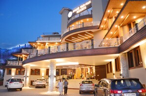 Un hotel de varios pisos con un letrero llamativo, una entrada curva y varios coches estacionados frente a él.