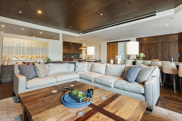 A modern living room with a sectional sofa, a wooden coffee table, and a kitchen in the background.