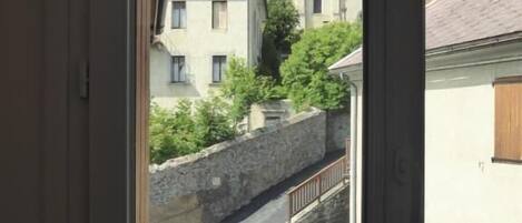 A view through a window of a street with buildings, a stone wall, and a church tower.