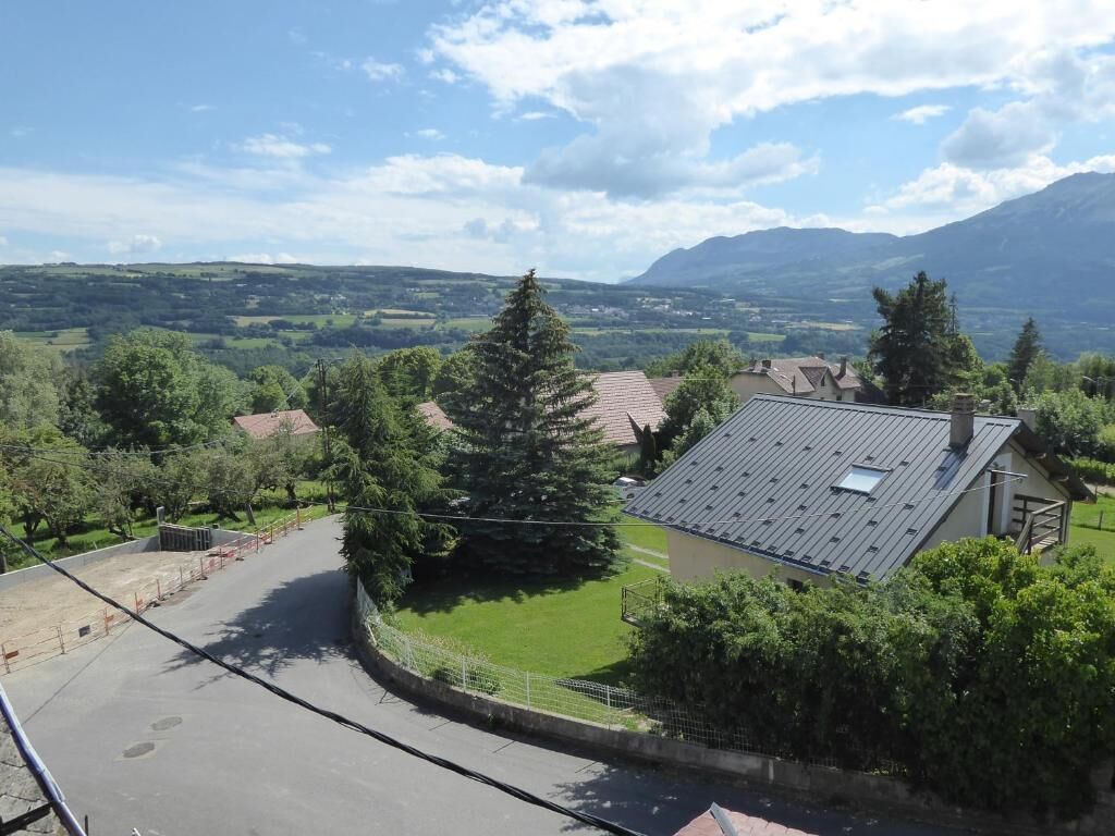 Zona residencial con una casa de techo inclinado, rodeada de vegetación y con vista despejada a colinas distantes.