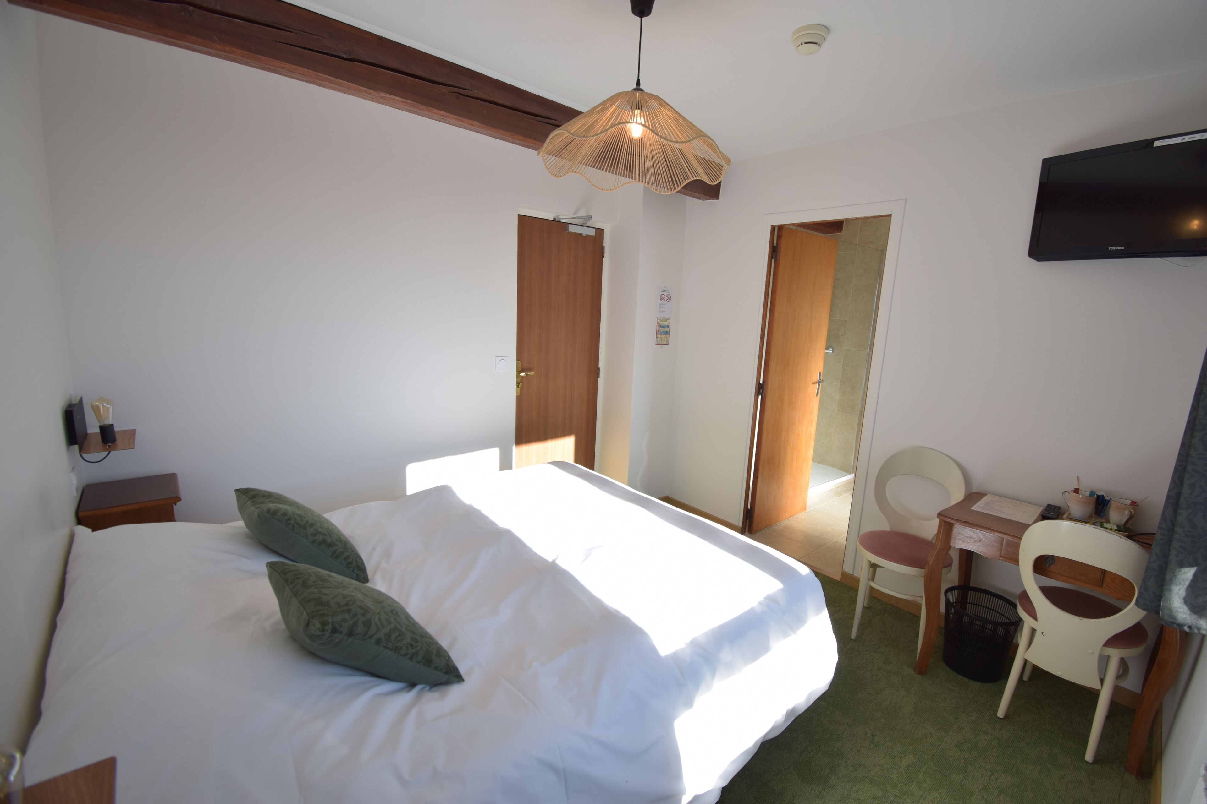 Un dormitorio con cama, mesita de noche, lámpara y televisor en la pared.