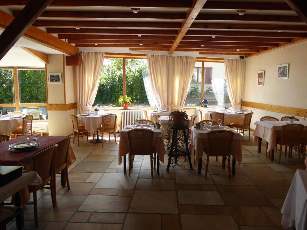 A dining area with multiple tables and chairs, large windows with curtains, and a tiled floor.