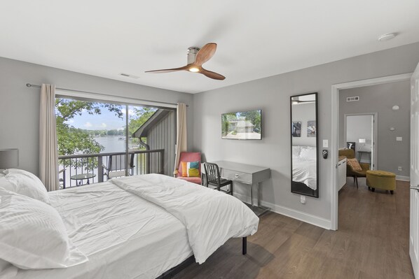 Une chambre à coucher comprenant un lit, un bureau, une chaise, un miroir et un balcon donnant sur l’extérieur.
