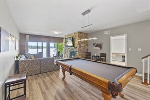 Une table de billard dans une pièce avec un mur en pierre, un plancher en bois et une vue sur l’extérieur.