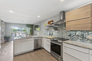 Une cuisine moderne avec des meubles blancs, une hotte en acier inoxydable et un grand îlot central doté d’un lave-vaisselle intégré.