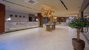 A hotel reception area with a marble counter, pendant lighting, and a large potted plant. - Aletris Deluxe Hotel & Spa (Manavgat)