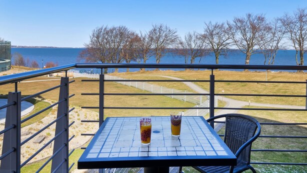 Un balcon avec une table et des chaises, donnant sur une étendue d’eau et des arbres.