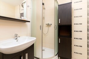 Ein Badezimmer mit weißem Waschbecken, einer Duschkabine aus Glas und dunklen Holzschränken.