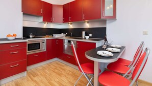 Une cuisine moderne avec des meubles rouges, un plan de travail noir et un coin repas avec des chaises rouges.