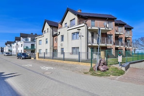 Un edificio residencial de varios pisos, con entrada protegida por un portón y cielo despejado.