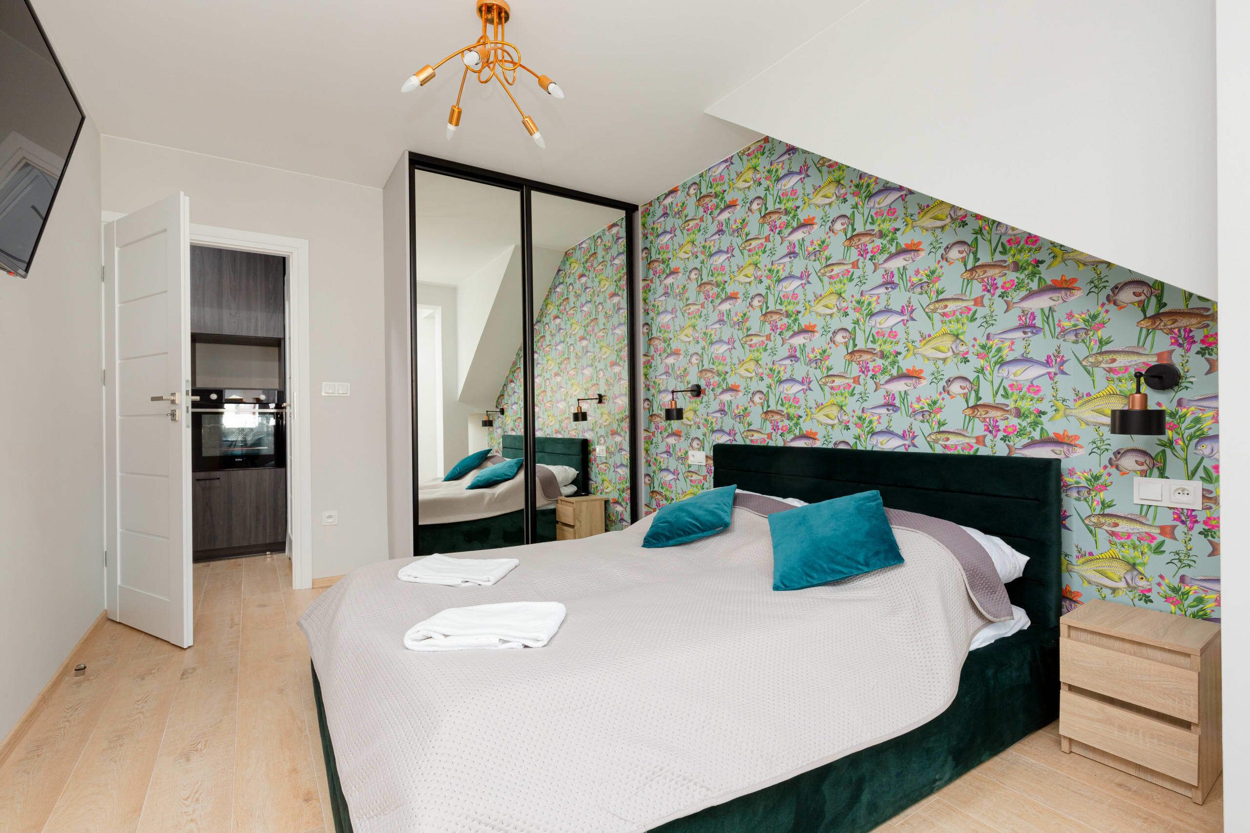 A bedroom with a bed, a bedside table, a mirror, and a wall with a fish pattern.