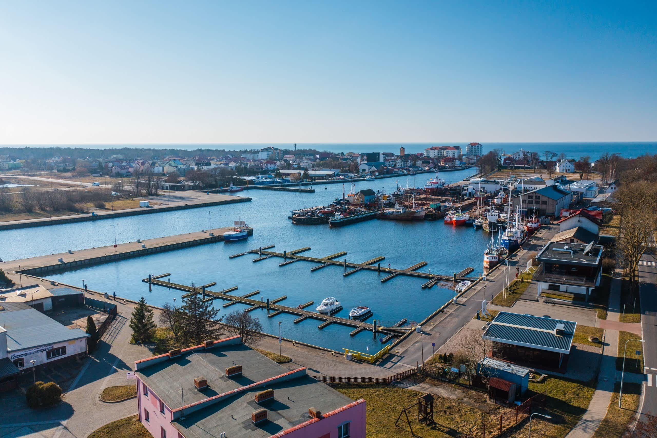 Een jachthaven met aangemeerde boten, een heldere lucht en gebouwen op de achtergrond.