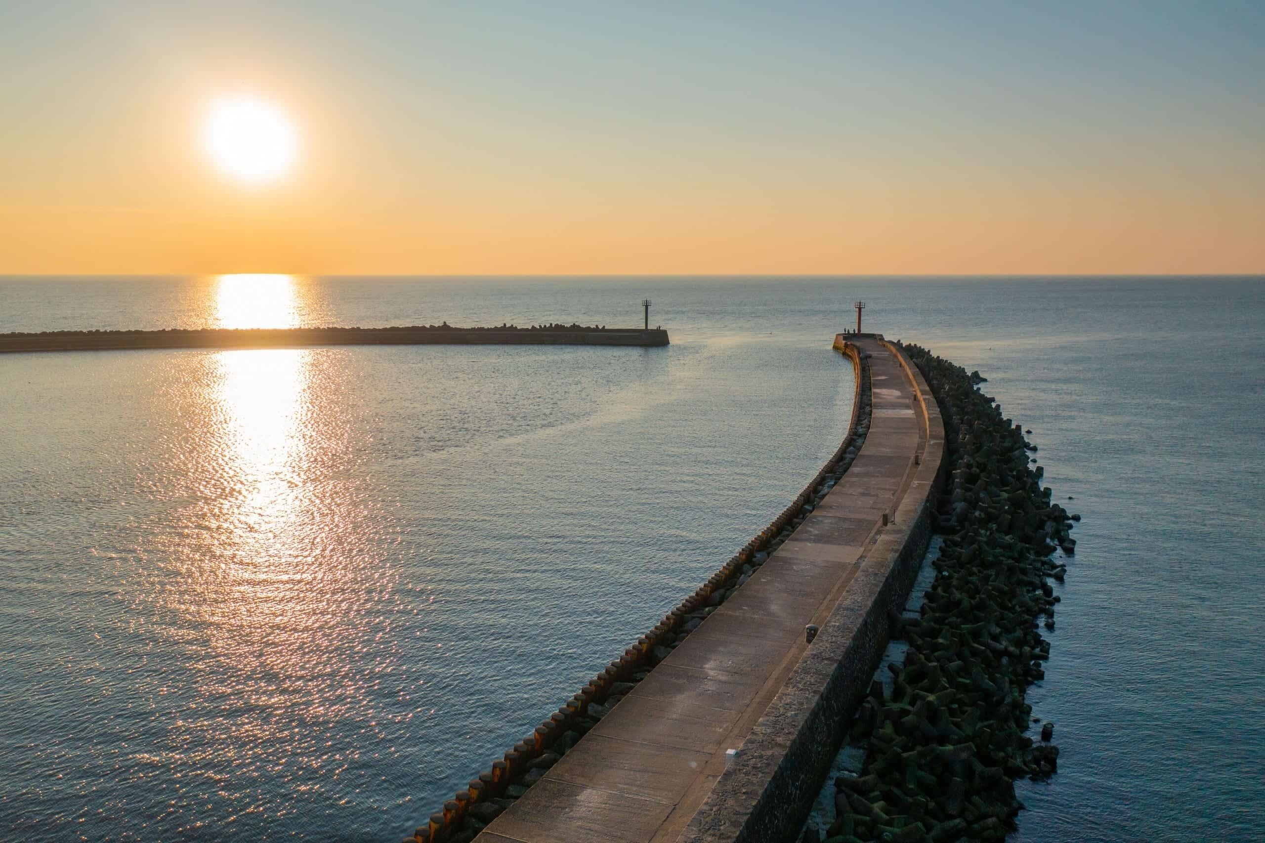 Une promenade en bord de mer qui s’avance dans la mer, avec un phare visible au loin.