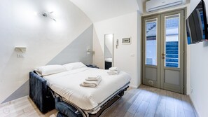 A modern bedroom with a bed, a bedside table, a mirror, and a TV mounted on the wall. - Italianway - The B Village Standard - T2 (Milan)