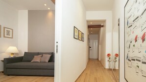 A hallway with a grey sofa, framed pictures on the walls, and a wooden floor.