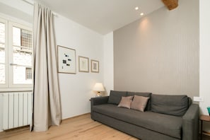 A living room with a grey sofa, a lamp, and framed pictures on the wall.