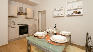 A modern kitchen with white cabinets, a built-in oven, and a dining area with a glass table set for four.