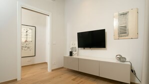 A modern living room with a flat-screen TV mounted on the wall, a white entertainment unit, and a wooden floor.