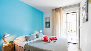 A neatly made bed with a green bedspread, a red towel, and a small plant on a bedside table. - PALAIS LIBERTE V AP4267 By Riviera Holiday Homes (Niza)