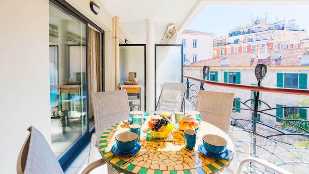 A balcony with a table set for dining, chairs, and a view of buildings. - PALAIS LIBERTE V AP4267 By Riviera Holiday Homes (Niza)
