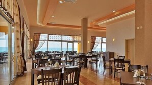 A spacious dining area with multiple tables and chairs, large windows offering a view of the sea, and a modern interior design. - Aheloy Palace Apartments (Pomorie)