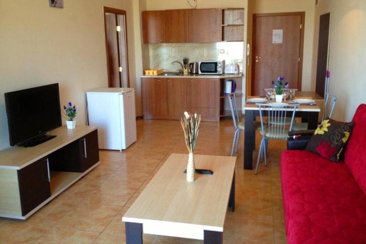 Un espacio habitable pequeño con televisor, un refrigerador compacto, una mesa de comedor y un sofá rojo.