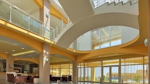 A spacious lobby with a high ceiling, glass railings, and large windows offering views of the outdoors. - Aheloy Palace Apartments (Pomorie)