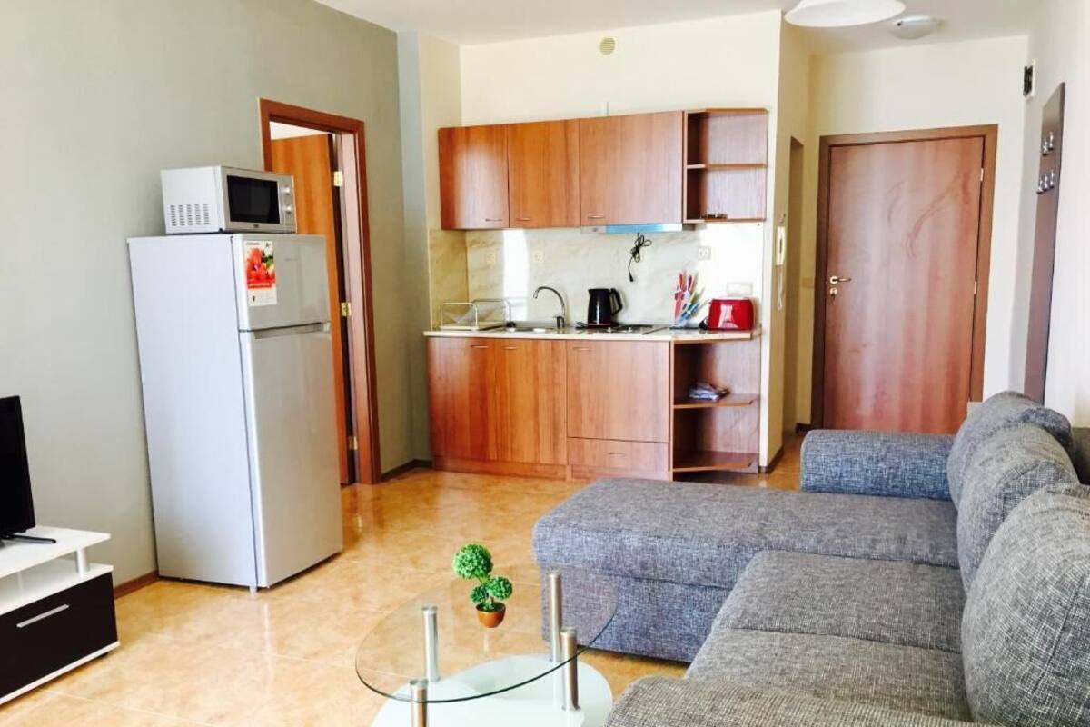 Un espacio habitable compacto con kitchenette, sofá gris y una pequeña mesa de vidrio.